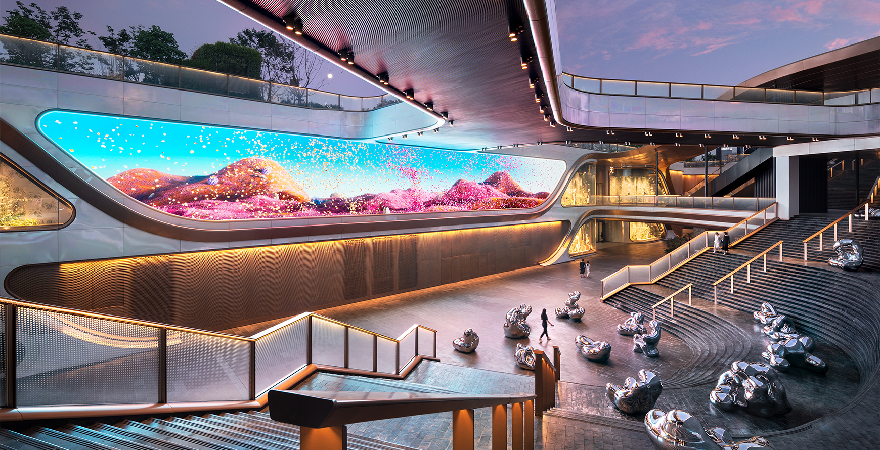SKP Chengdu sunken plaza with a sweeping digital façade, sculptural seating, tiered steps and elevated walkways at dusk.