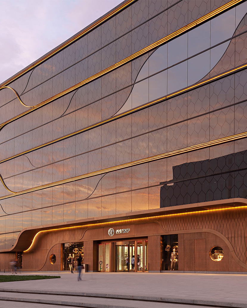 The SKP Xi’an façade translates the SKP Curve into a luminous urban frontage, with bronze-toned detailing, reflective glass and illuminated horizontal lines creating a distinctive retail landmark at dusk.